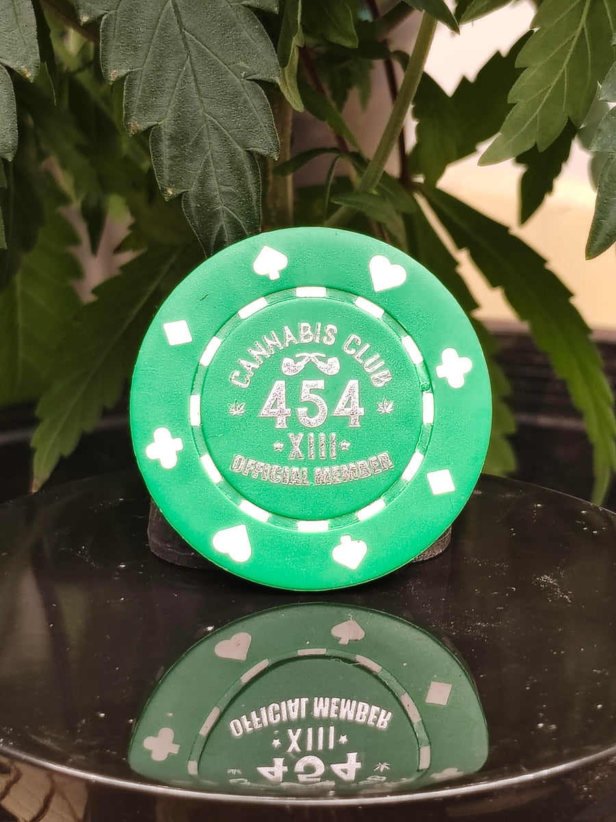 Green poker chip with white card-suit inlays, labeled 'Cannabis Club 454', on a black surface with cannabis leaves.