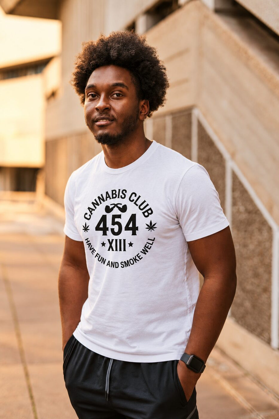 Man with curly hair against a sunlit concrete wall, wearing a Cannabis Club 454 seal tee